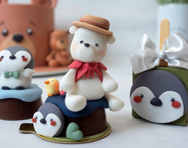 Doces individuais com ursinhos e pinguins modelados à mão em pasta americana, um deles com chapéu de palha e lenço vermelho