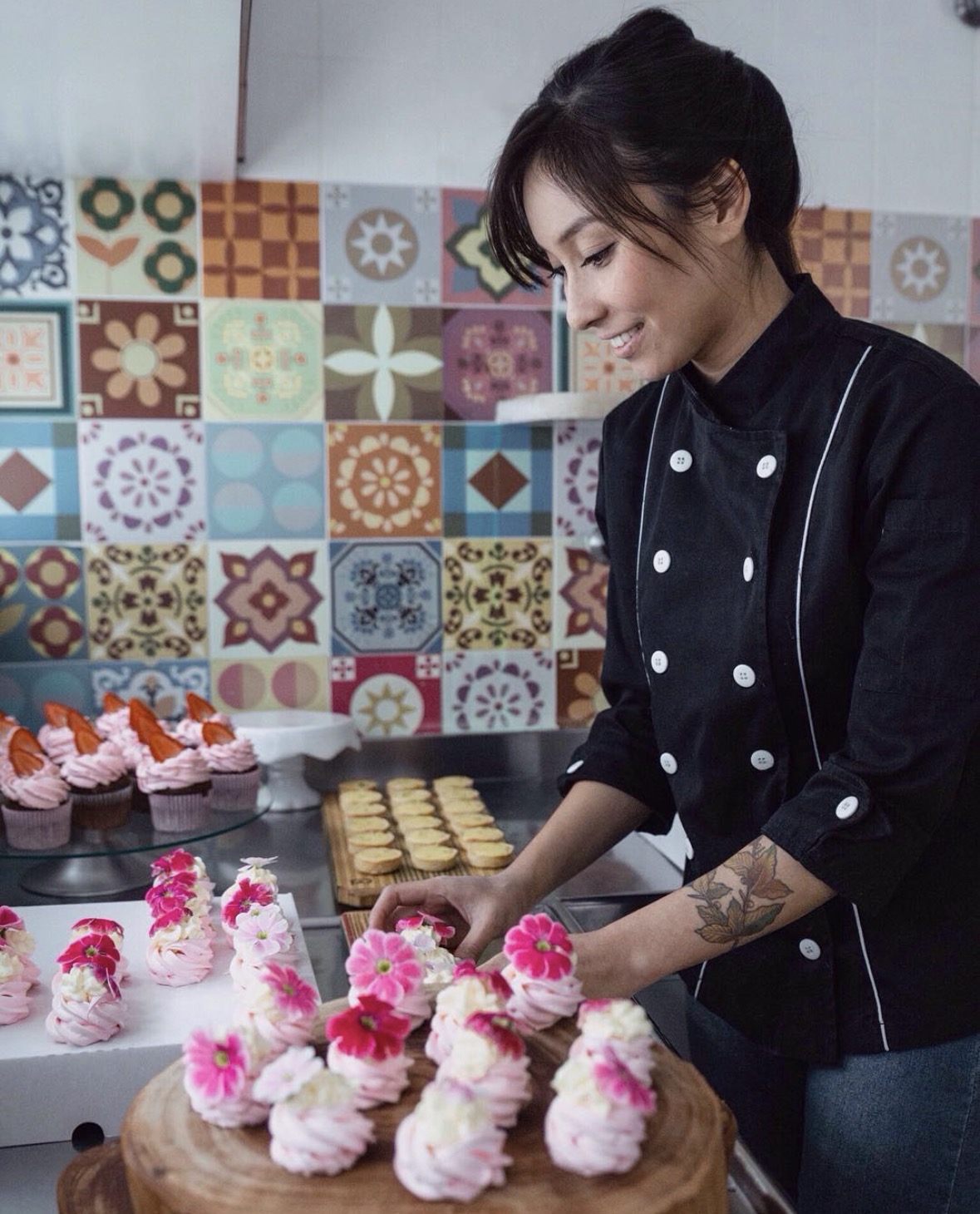Deborah Tami finalizando doces cor-de-rosa com flores em uma bancada de confeitaria para evento