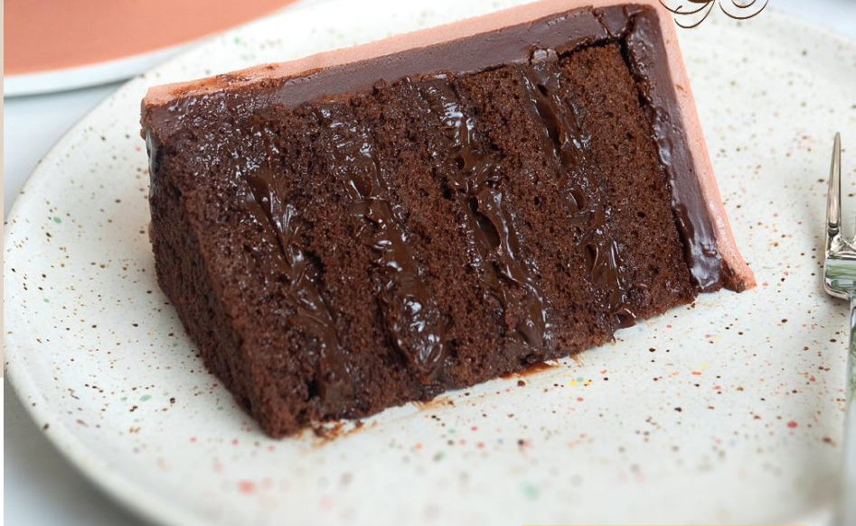 Fatia de bolo de massa de chocolate em camadas com recheio de brigadeiro belga escorrendo, em prato de cerâmica salpicada