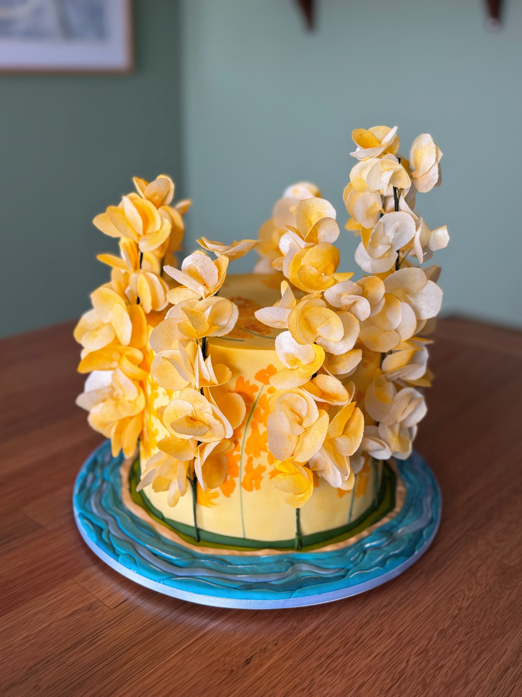 Bolo amarelo com pintura à mão e cascata de flores de wafer paper em tons de amarelo e creme, sobre base pintada imitando água