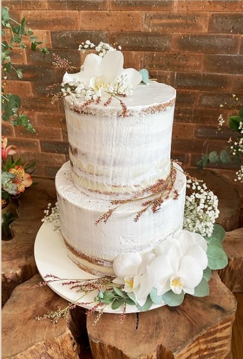Bolo de casamento de dois andares em naked cake com orquídeas brancas, mosquitinhos e eucalipto, sobre tronco de madeira